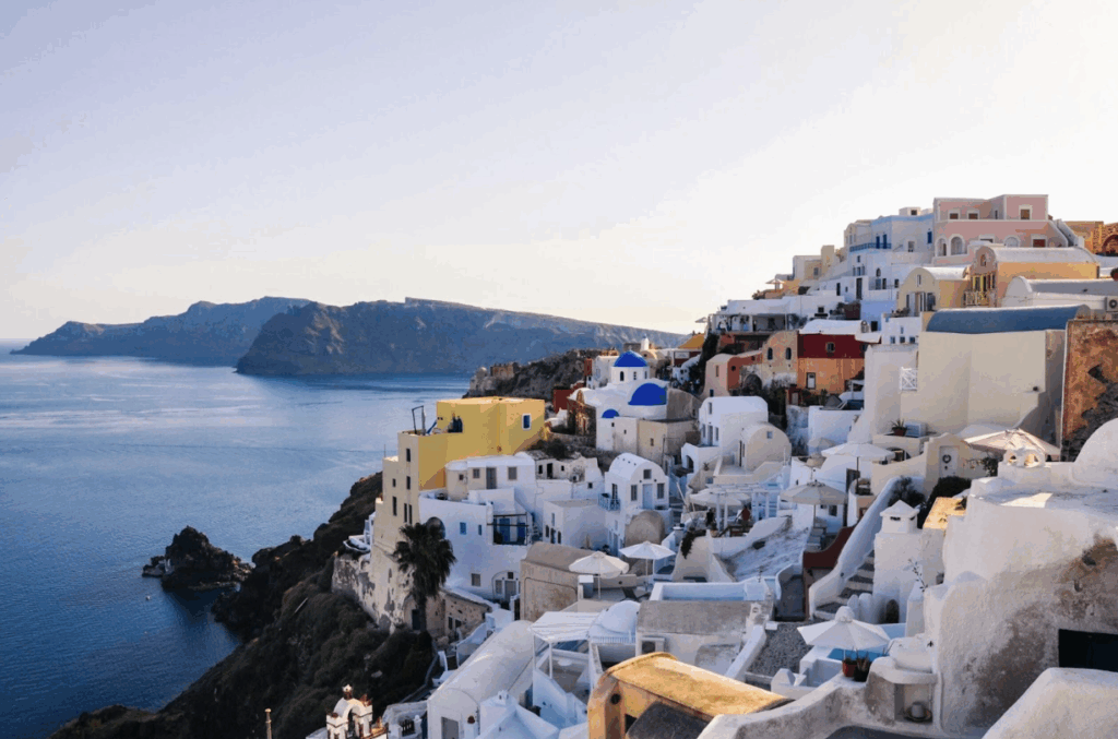 a white buildings on a hill by the water with Santorini in the background