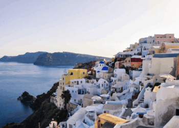 a white buildings on a hill by the water with Santorini in the background
